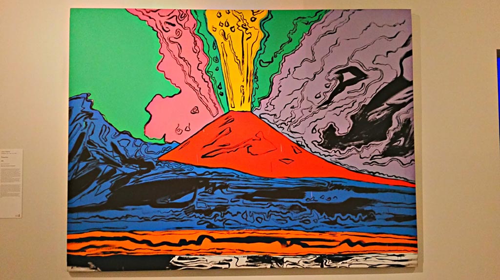 Vesuvius, acrylic on screen, painted by Andy Warhol (Pittsburgh, 1928 – New York, 1987), in 1985.
On display in exhibition “Pompei e Santorini” in Rome, 2019. Photo courtesy of Giuseppe Ciaramella.
According to the information card –
“In 1985, the Neapolitan art dealer Lucio Amelio organized a show of work by Andy Warhol in the Museo di Capodimonte entitled Vesuvius.
For the occasion, the artist developed a Pop revisitation of the volcano in a series of screenprints whose bright colours alter the drama of the eruption in an unprecedented cartoon-like vision. Like many artists, Warhol fell under the sublime spell of Vesuvius, the best-known landmark of the Neapolitan landscape. As he wrote – “Vesuvius for me is something much greater than a myth. It is terribly real.”